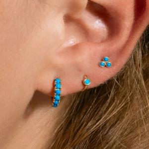 Detailed view of three turquoise gold earrings worn on ear, including hoop and stud styles