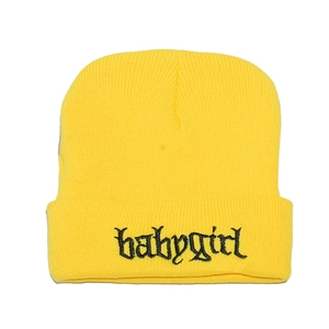 Dettaglio ravvicinato del berretto in maglia gialla con ricamo babygirl nero corsivo