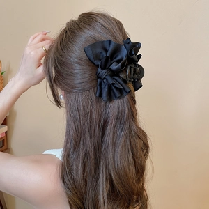 Detail of elegant black layered fabric bow hair claw clip worn on a woman's hair