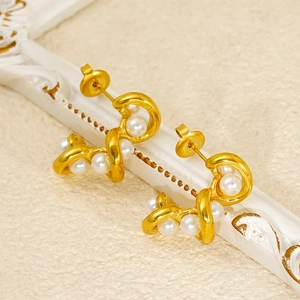 Dettaglio di orecchini a cerchio dorati ritorti con perle su cornice vintage
