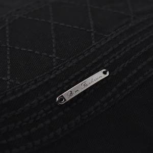 Detail of black diamond-quilted cotton fabric with a silver Bem Fashion metal nameplate