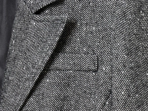 Detailed view of herringbone tweed blazer lapel and pocket with textured fabric weave