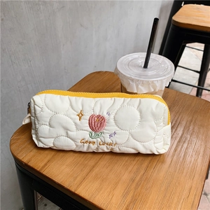 Close-up of quilted white pencil case with tulip embroidery and yellow zipper detail