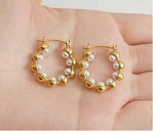 Détail de boucles d'oreilles dorées 18 carats avec perles blanches sur la main