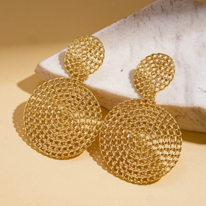 Détail de boucles d'oreilles géométriques dorées posées sur un socle en marbre blanc