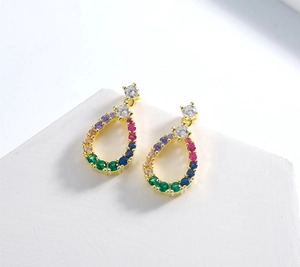 Detail of teardrop hollow gold earrings with multicolored zircon pavé on a white stone base