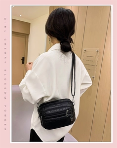 Détail d'un sac bandoulière noir texture crocodile avec plusieurs poches zippées porté