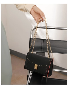 Detail of black leather crossbody bag with gold rivets and contrasting red edge oiling