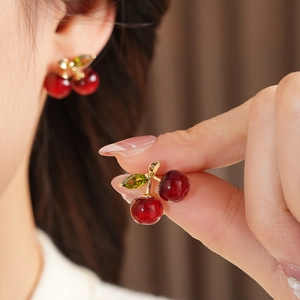 Close-up of cherry stud earrings with red beads and green gemstone leaves on model