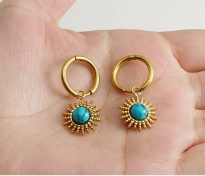 Close-up of golden sunflower earrings with turquoise stone held in palm for size scale