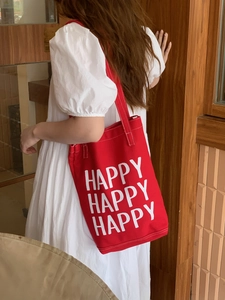 Detail of red canvas tote bag featuring white HAPPY print and sturdy stitched handles