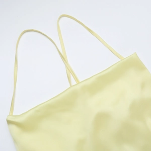 Gros plan sur la texture du tissu en satin jaune lisse et la fine bretelle de la robe