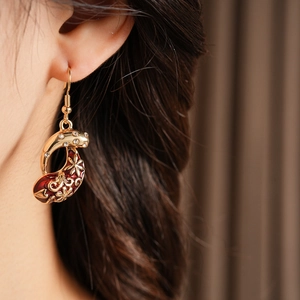 Macro shot of a vintage gold drop earring with red enamel and zircon on a model's ear