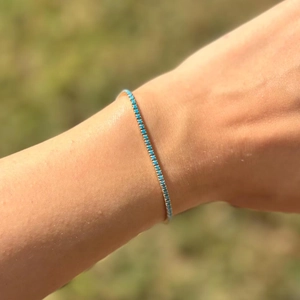 Detail showing a tennis bracelet with teal square-cut cubic zirconia in gold setting