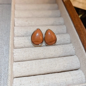 Gros plan des boucles d'oreilles orange en forme de larme sur un tapis de bijoux beige