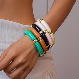 Dettaglio di braccialetti impilati in acrilico colorato con distanziatori dorati al polso