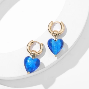 Gros plan de créoles dorées avec pendentifs cœur bleus sur un présentoir blanc épuré