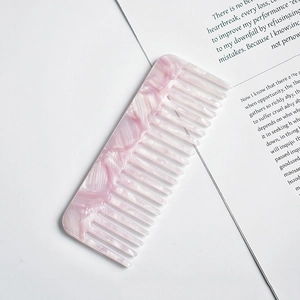 Detail of pink marble pattern wide-tooth acetate comb placed on an open book page