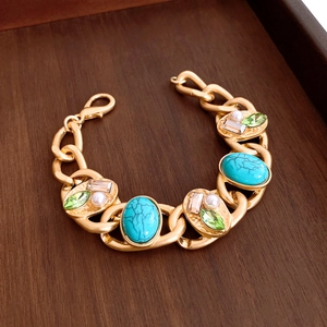 Detail eines Vintage Gliedarmbands in Gold mit Türkissteinen und Perlen auf Holz