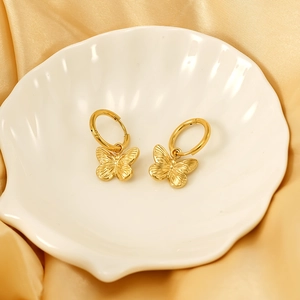 Detail of golden butterfly stud earrings with textured wings on a white shell tray