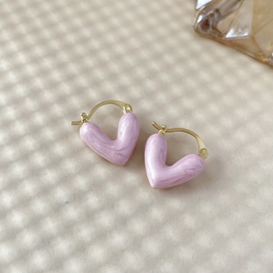 Détail de boucles d'oreilles cœur en émail rose marbré avec placage or sur fond texturé