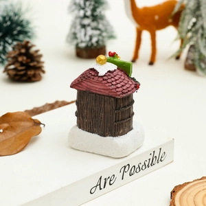 Détail d'une maison de Noël miniature en résine avec toit rouge sur un plateau blanc
