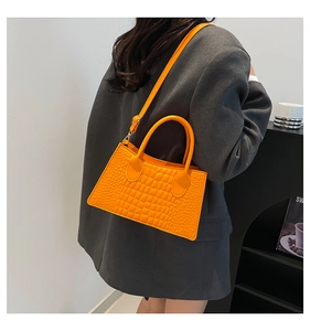 Modell mit oranger Handtasche in Krokodil-Optik, goldenen Beschlägen und Schultergurt