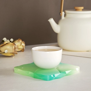Detail eines geometrischen grünen Harz-Untersetzers mit Facettenschliff und Teetasse