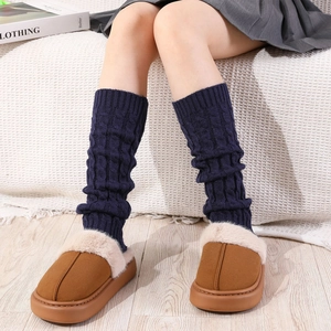 Close-up of navy blue cable knit leg warmers paired with plush faux fur house slippers