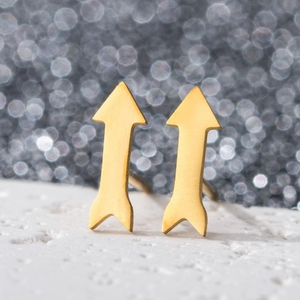 Macro shot of gold arrow-shaped stud earrings with brushed texture on a white surface