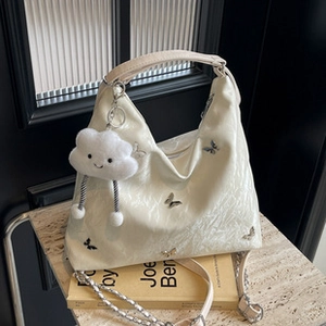 Dettaglio della borsa in pelle PU bianco crema con ricamo a farfalla e ciondolo a nuvola