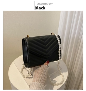 Detail of black crossbody bag with V-shaped quilting and elegant white pearl chain strap