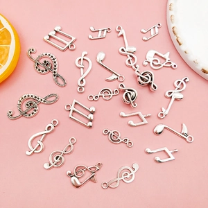 Close-up of silver musical note alloy charms for DIY jewelry on a pink surface