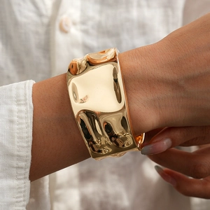 Close-up of a wide gold cuff bracelet featuring a molten liquid metal texture design