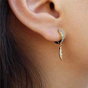 Detail of gold feather dangle earring with blue stone inlay worn by a model