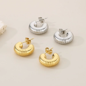 Detailed view of gold and silver stainless steel ribbed C-shaped earrings on stone
