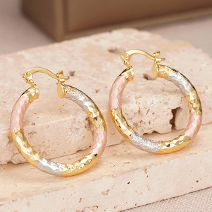 Macro detail of tri-color hoop earrings with diamond-cut texture on beige stone