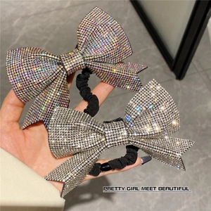 Detail of sparkling rhinestone bow hair ties with black pleated elastic bands in hand