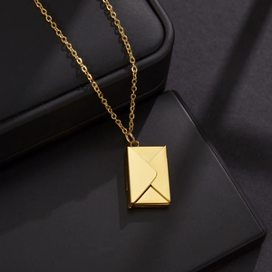 Macro shot of gold envelope locket pendant on a black jewelry box with cross chain