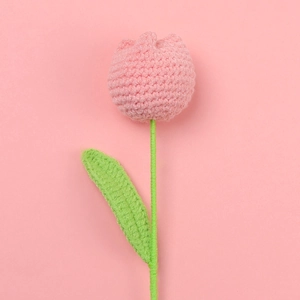 Macro shot of a pink hand-knitted tulip flower with green stem against a soft background