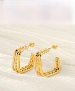 Macro detail of multi-layer geometric gold-plated earrings on white silk texture background