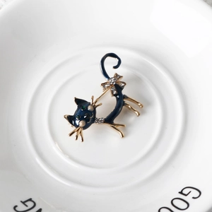 Detail view of cat brooch with blue enamel and pearl on white ceramic plate