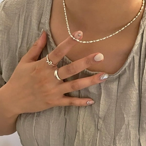 Detail of silver beaded necklace and minimalist rings styled on grey textured fabric