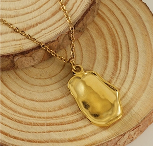 Macro detail of gold irregular rectangle pendant with lava texture on wood background