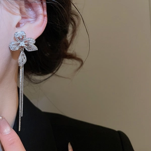 Macro shot of silver flower drop earrings with zircon tassel on model's ear