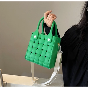 Detail of green woven EVA bag with white canvas shoulder strap held by hand