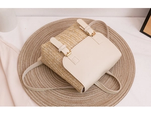Detail of beige woven straw backpack featuring leather flap and dual metal buckles