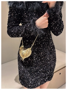 Detail of a gold heart-shaped shell bag with chain strap on a black sequin dress