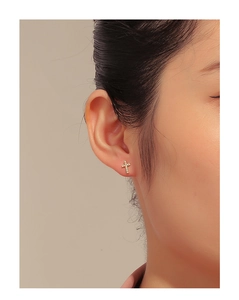 Close-up of a gold cross stud earring with micro-pave zircons on a model's ear