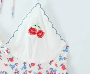 Detailed close-up of cherry embroidery and lace trim on a white floral halter dress